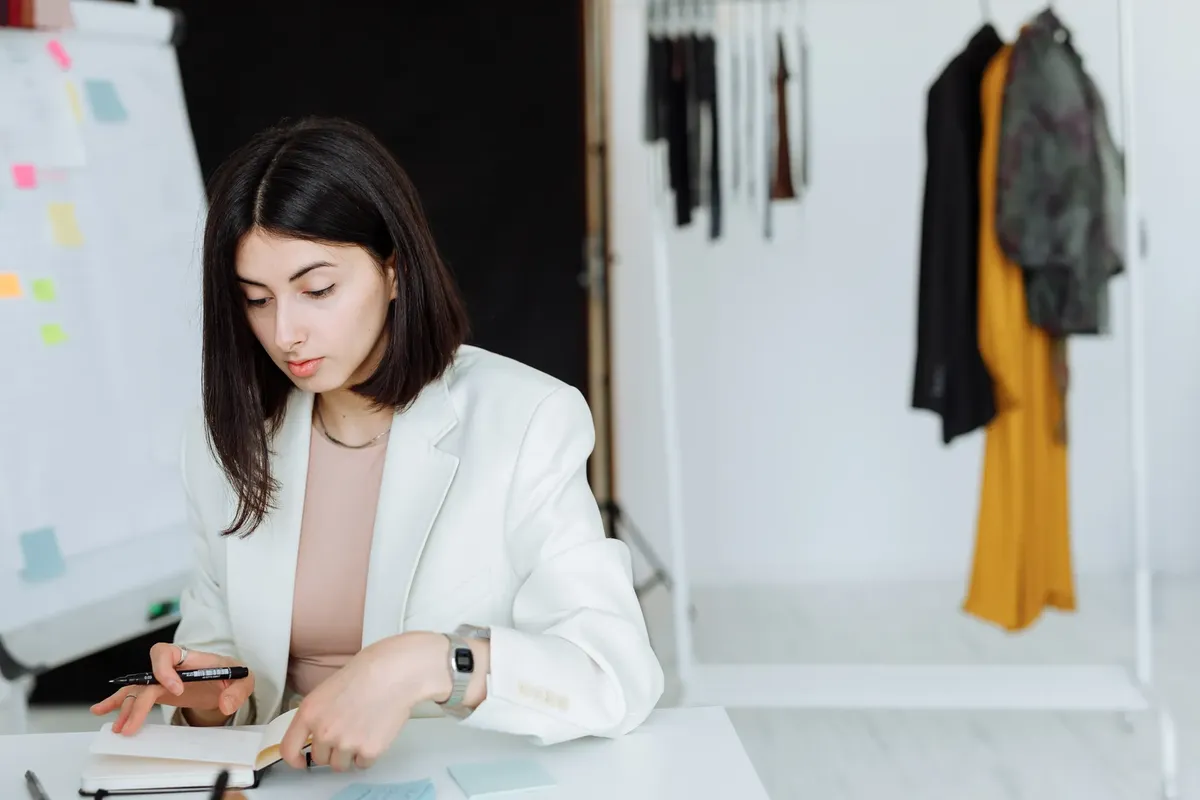 Young woman in white blazer writing notes in a modern fashion office. Stylish workspace.