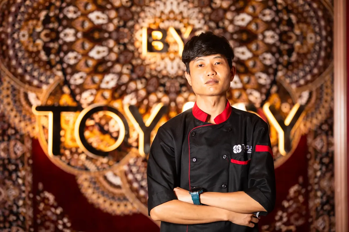 Professional chef posing confidently in a beautifully decorated restaurant interior with intricate designs.