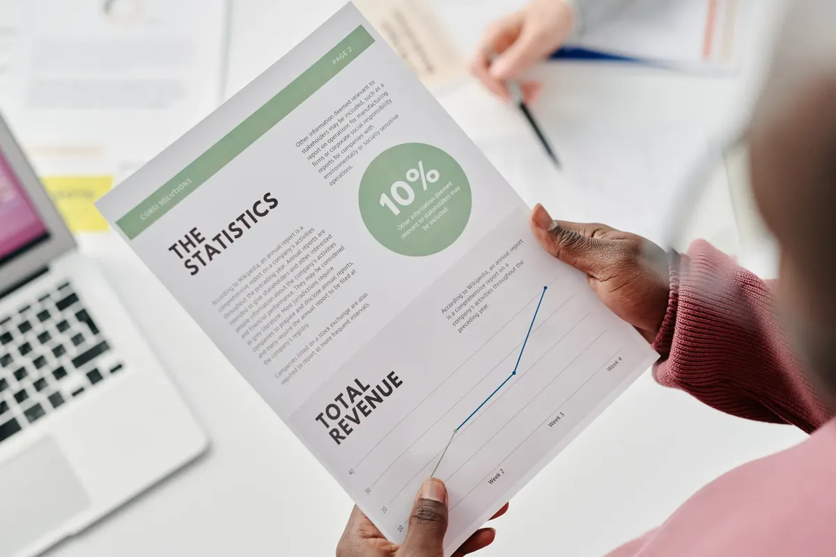 Hands holding a statistical report during a business meeting. Includes revenue graphs and analysis.
